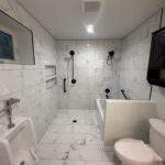 Modern bathroom with marble tile, urinal, accessible tub, black fixtures, and toilet.