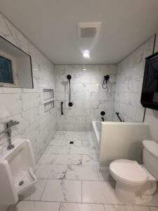 Modern bathroom with marble tile, urinal, accessible tub, black fixtures, and toilet.