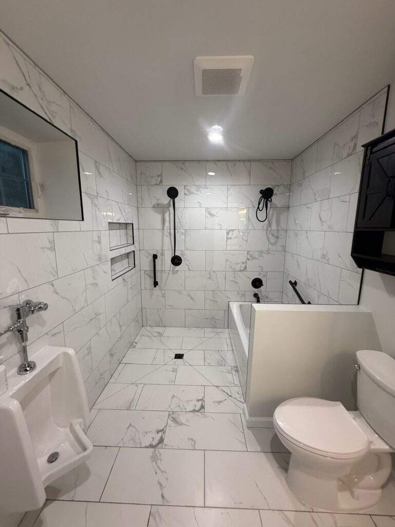 Modern bathroom with marble tile, urinal, accessible tub, black fixtures, and toilet.