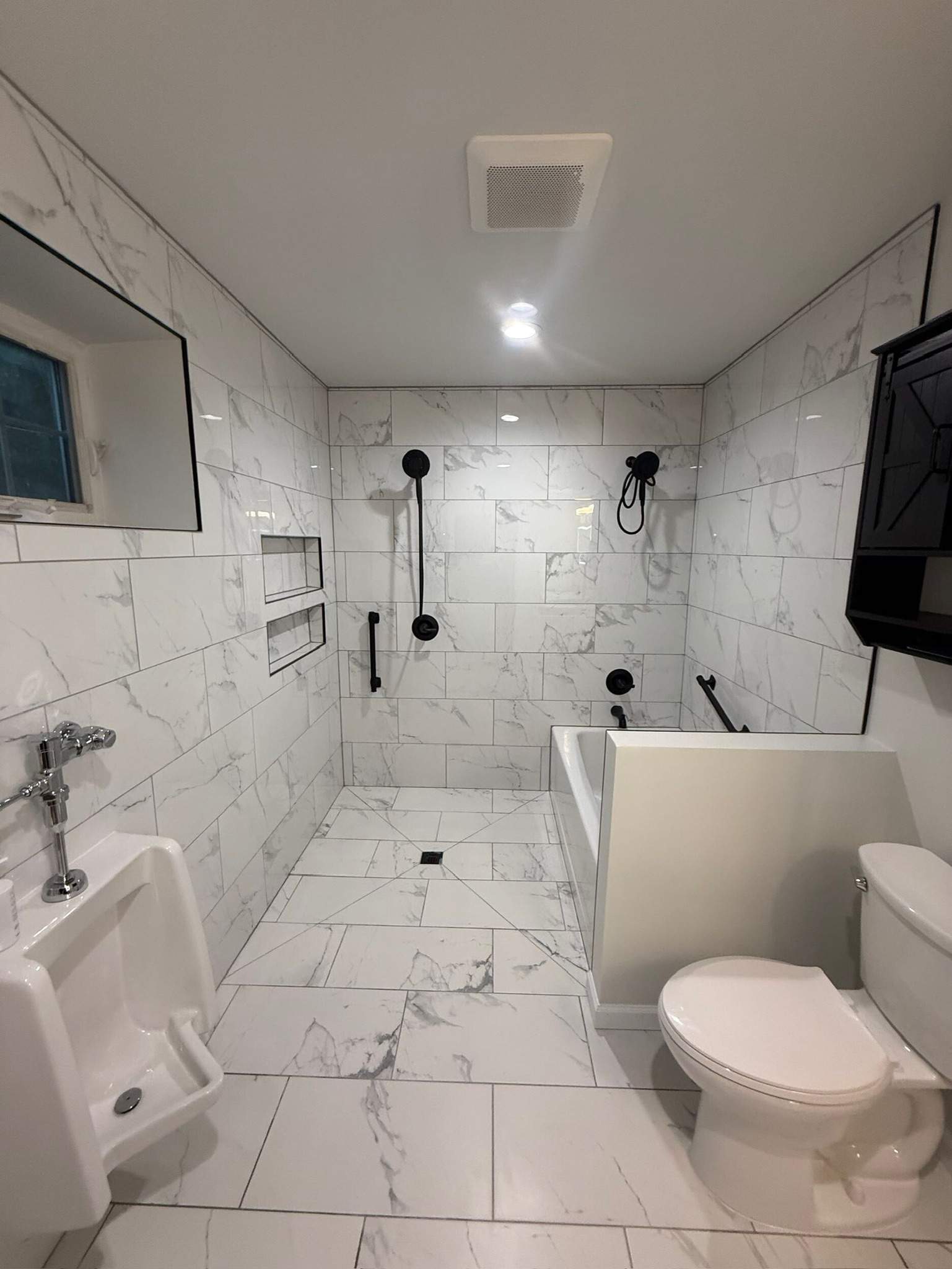 Modern bathroom with marble tile, urinal, accessible tub, black fixtures, and toilet.