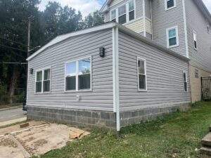Gray vinyl siding on a house addition with block foundation.