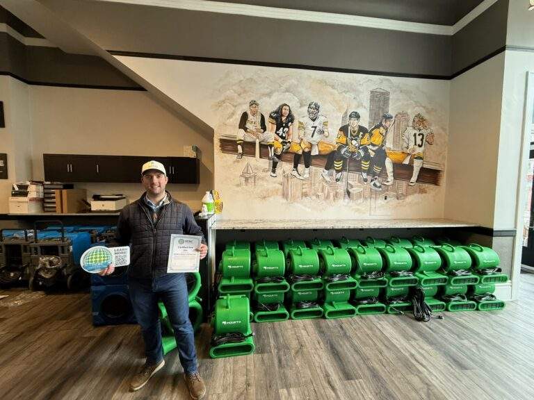 Man holding IICRC certification in front of water damage restoration equipment.