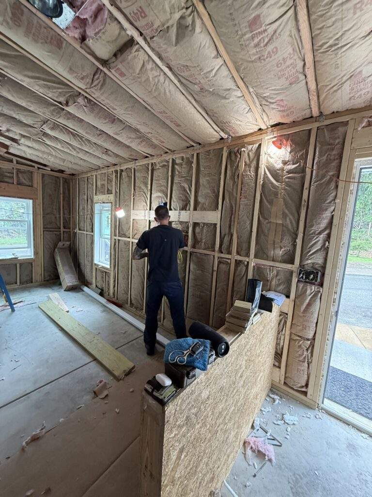 Man working on framing and insulation in a room under construction. R49 fiberglass insulation visible.