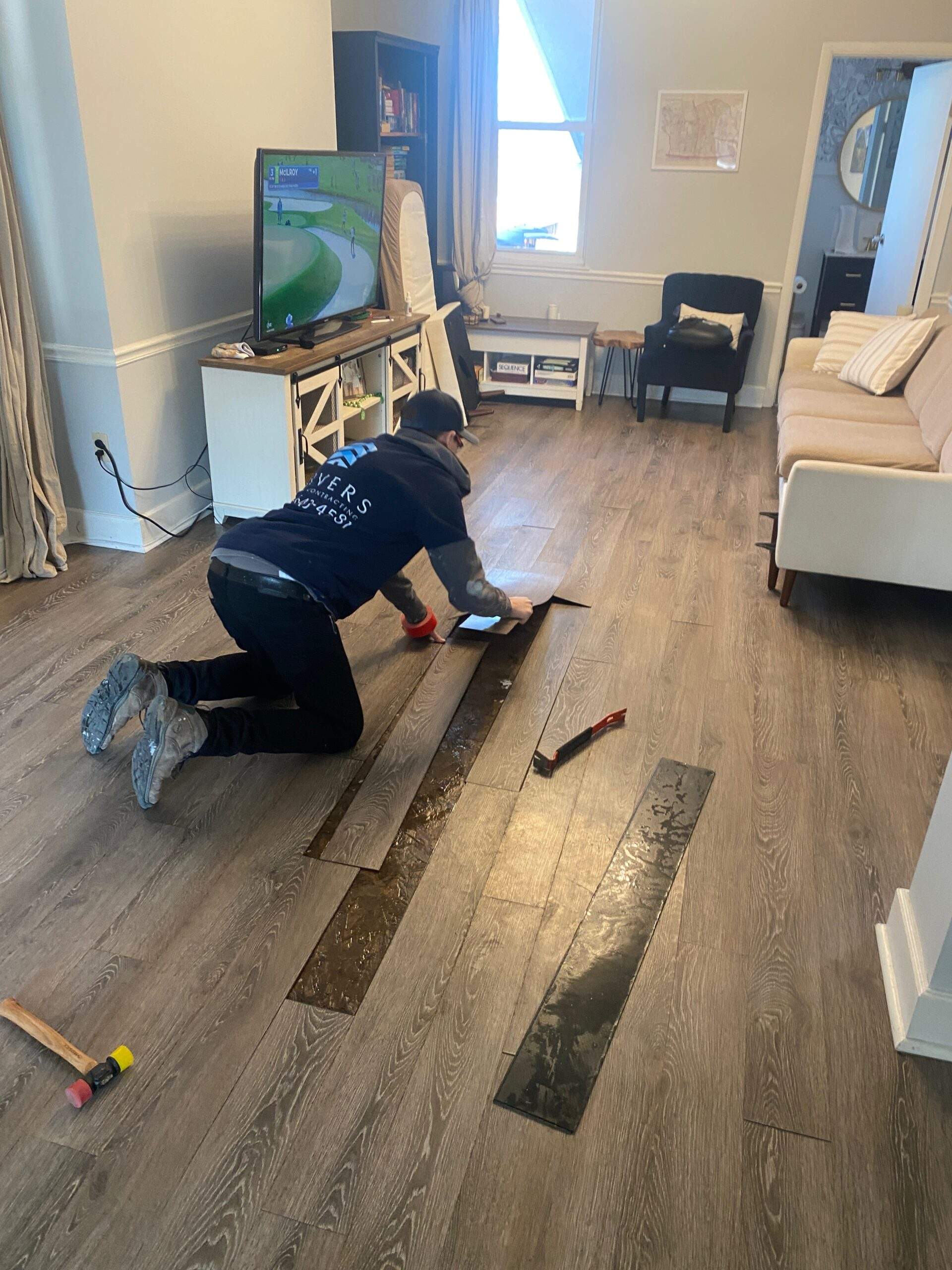 Man installing new wood-look flooring in a living room.