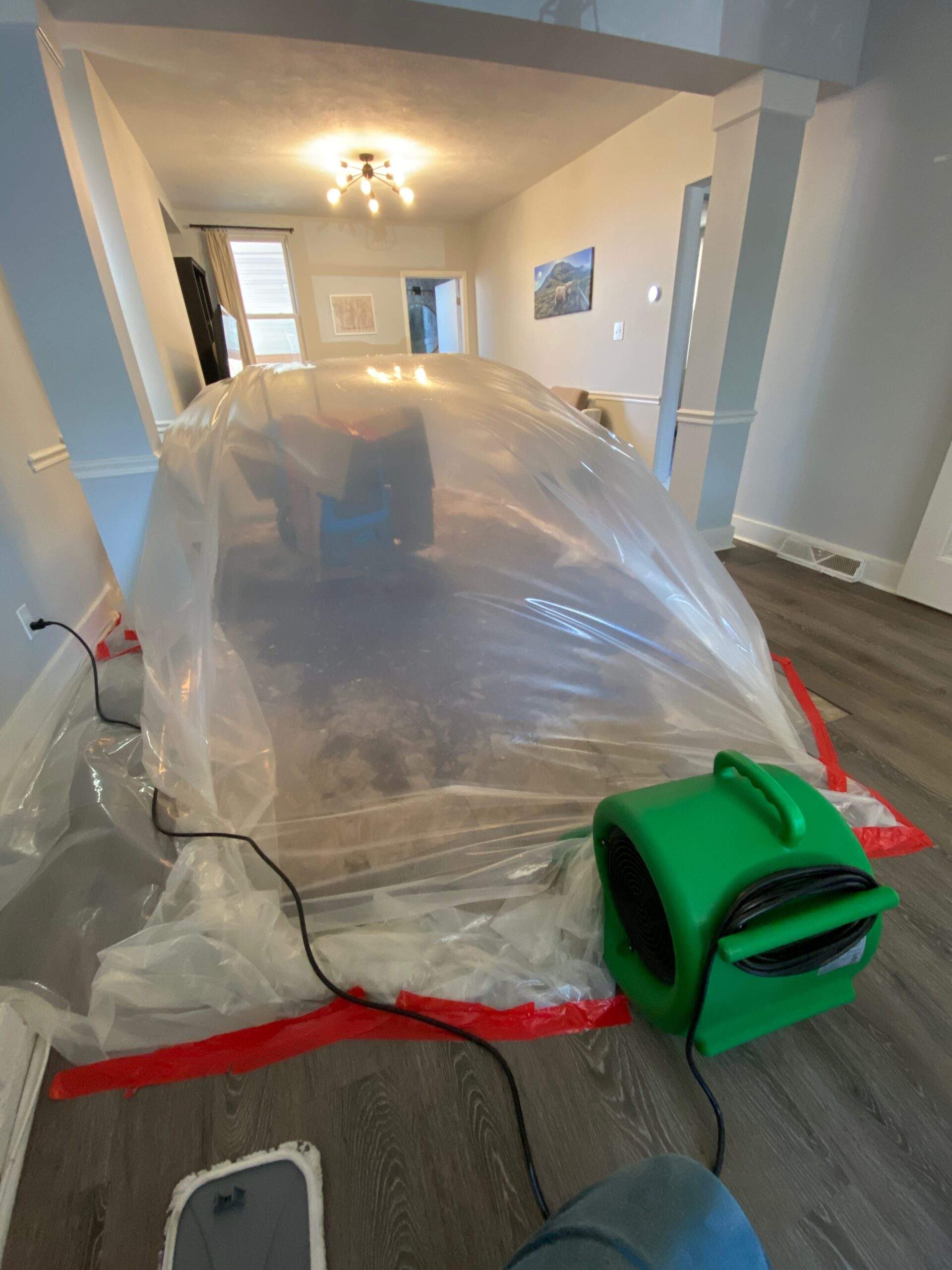 Drying equipment under plastic sheeting in a room, likely related to home additions work.