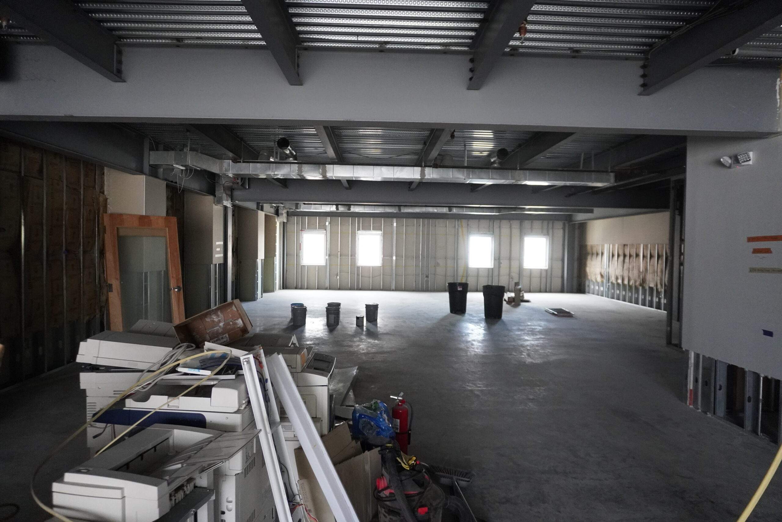 Construction site office with unfinished walls, concrete floor, and discarded office equipment.