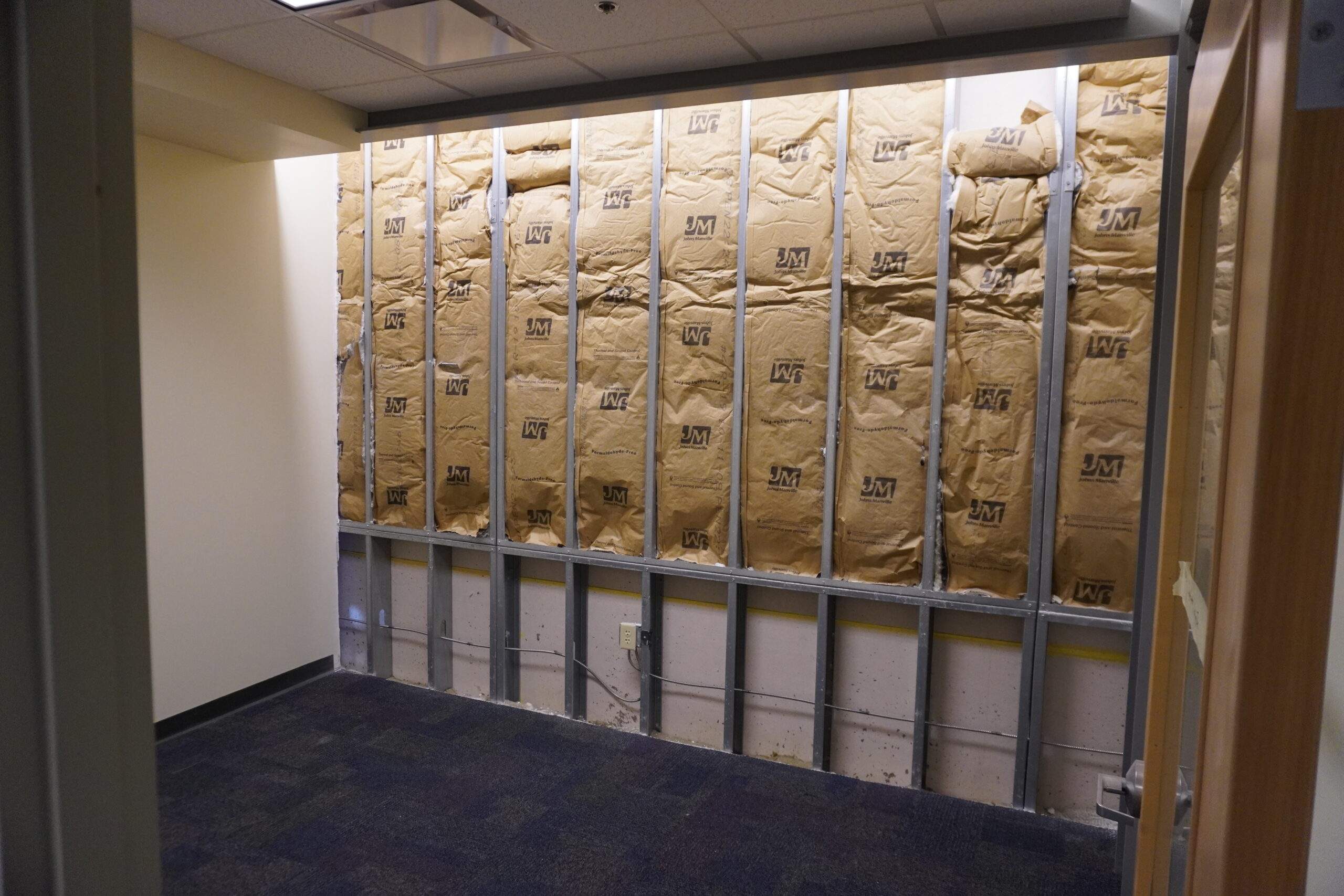 Office wall under construction with insulation and metal studs.