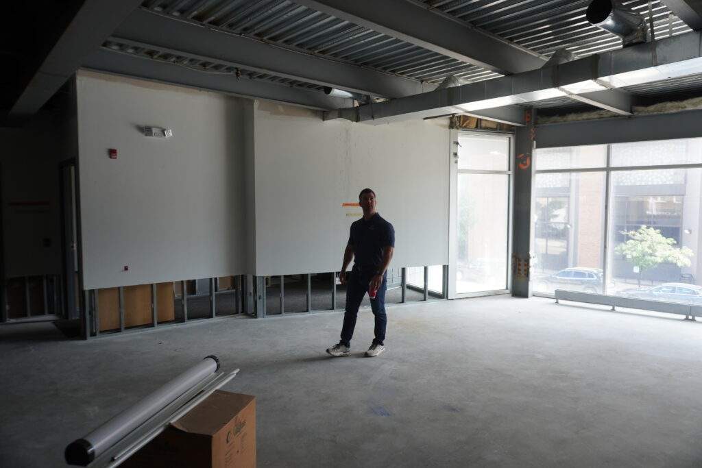 Man standing in unfinished commercial space with exposed beams and windows