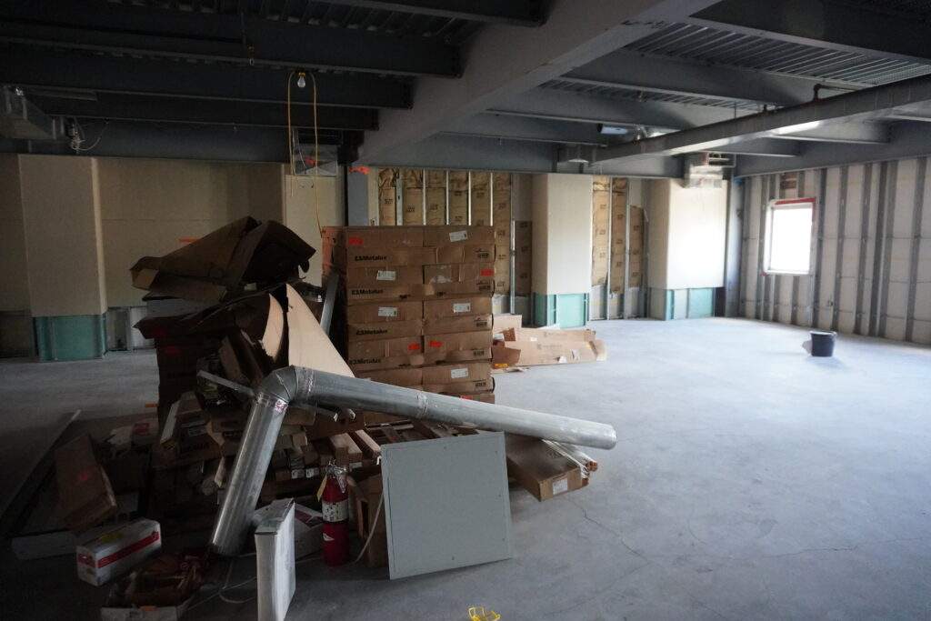 Construction site interior with stacked boxes, metal ductwork, and unfinished walls.