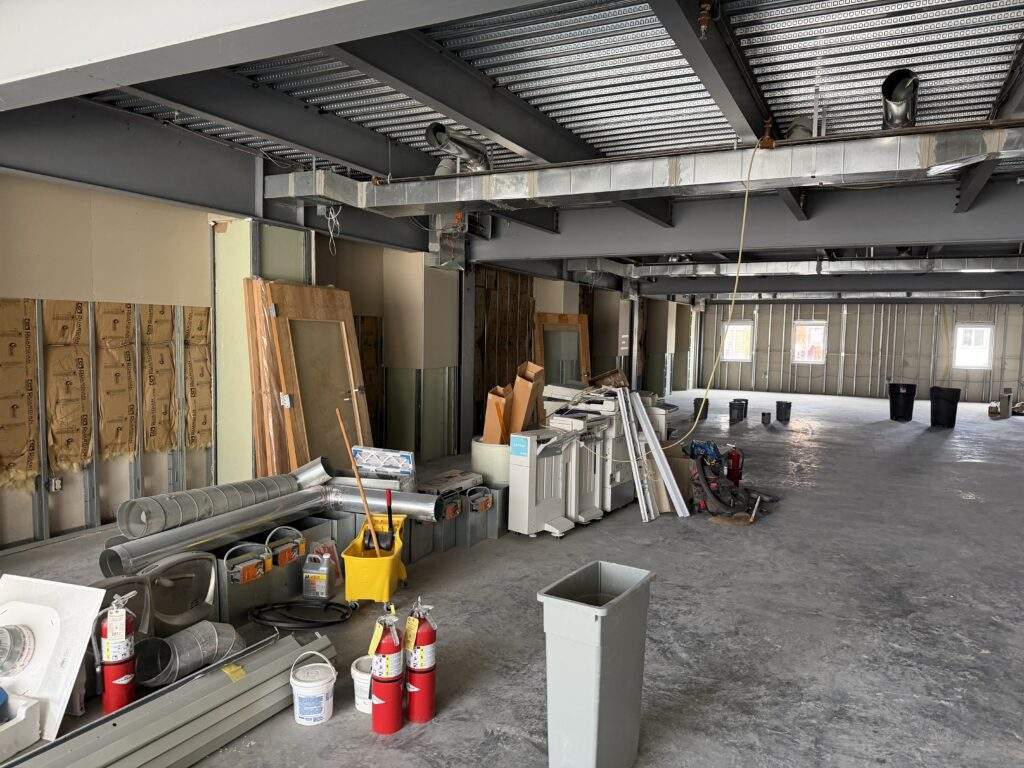 Construction site interior with exposed framing, ductwork, and building materials.