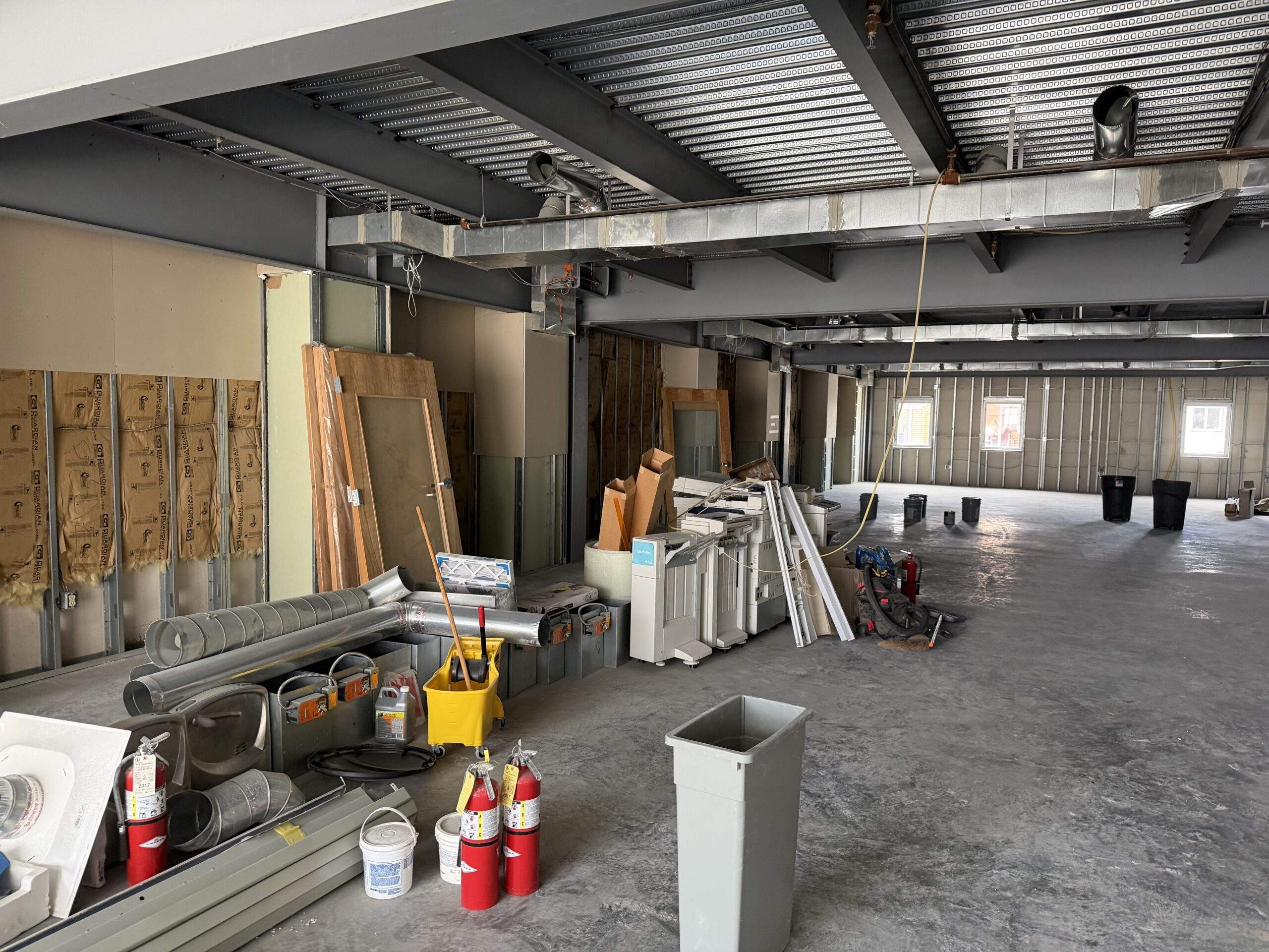 Construction site interior with exposed framing, ductwork, and building materials.
